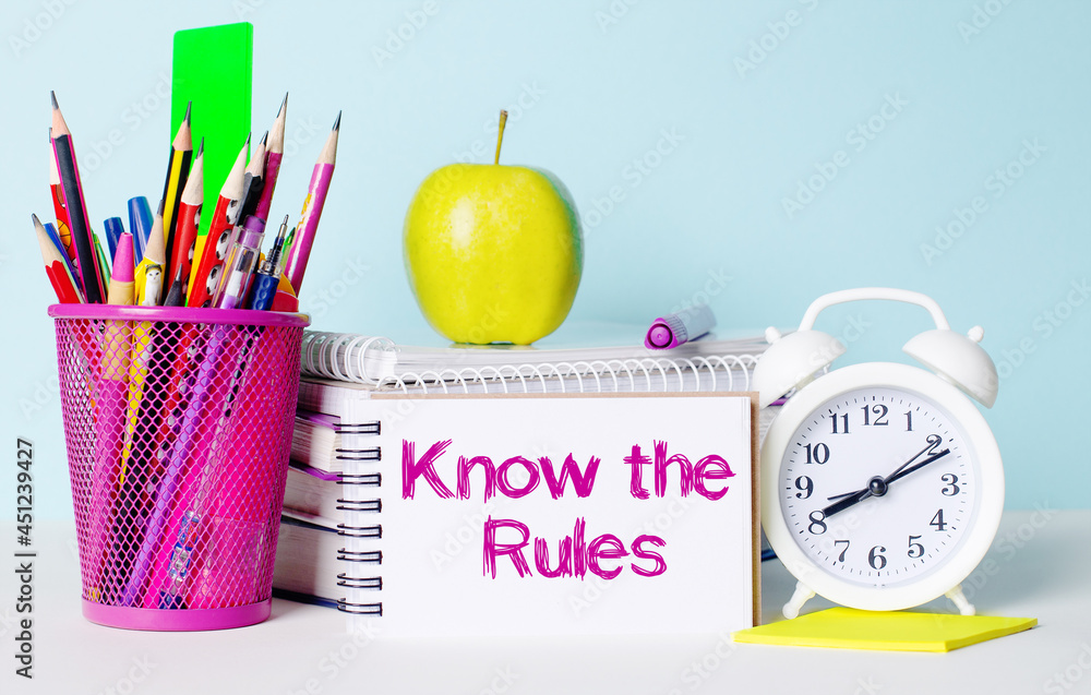 Poster on a light table there are books, stationery, a white alarm clock, an apple. next to it is a noteboo