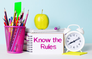 On a light table there are books, stationery, a white alarm clock, an apple. Next to it is a...