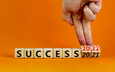 Planning 2022 success new year symbol. Businessman turns a wooden cube and changes words success 2021 to success 2022. Beautiful orange background, copy space. Business, 2022 success new year concept.