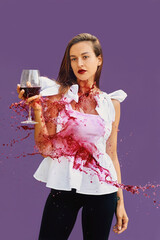 Calm attractive woman in white blouse with glass of red wine in her hands in red wine splashes....