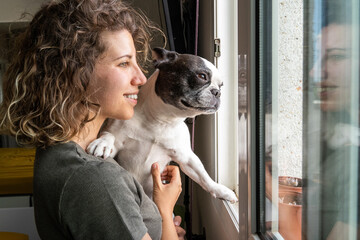 Young caucasian woman with bulldog at home. Horizontal view of woman holding baby dog in the window.