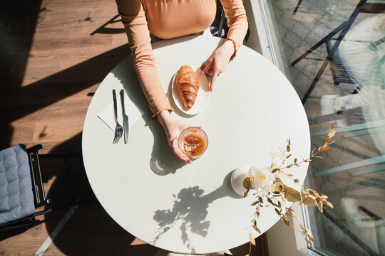 Anonymous Woman with coffee and croissant at table in cafe