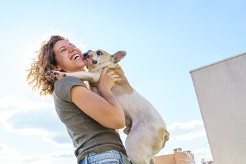 Happy woman dog lover holding baby bulldog. Horizontal view of woman with pet. Lifestyle with animals outdoors.