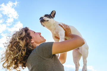 Happy woman holding up a bulldog. Horizontal view of woman with pet outdoors. Lifestyle with animals