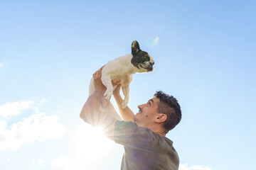 Happy man holding up a bulldog. Horizontal view of man with pet outdoors. Lifestyle with animals