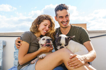 Happy young couple playing with dog outdoors. Horizontal view of couple laughing with bulldog on couch.