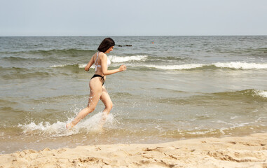 Fototapeta na wymiar young beautiful girl running along the sand of the sea shore