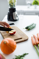 partial view of woman cutting apple near blurred pumpkin and carrots on table.