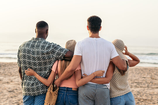 Group of anonymous multiethnic friends embracing on seashore in sunset