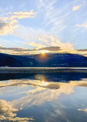 sun setting over the mountains with the reflection in the fjord, midnattsol.