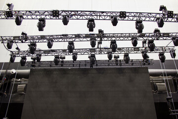 Moving head spotlight devices are clamped on a rigging steel trusses. Video led screen....