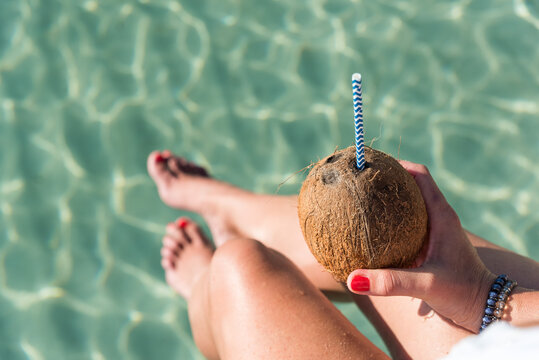 Crop woman with coconut drink near sea in summer