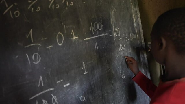 Black African boy and white volunteer writing numbers on the board of school. Volunteering education program of an NGO. 4K.