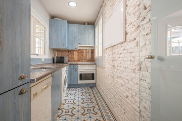 Blue kitchen cabinets with wood grain and white appliances, an exposed white brick wall and...