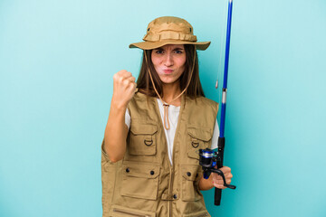 Young caucasian fisherwoman isolated on blue background showing fist to camera, aggressive facial expression.