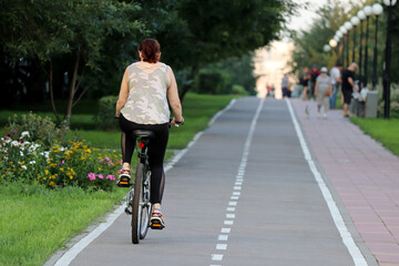 Woman in sports leggings riding on a bicycle on a path in a green park. Girl cyclist, summer leisure, cycling concept