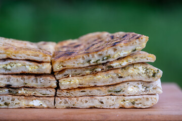 Pieces of baked dough tortilla with cottage cheese and herbs on a wooden table, close up