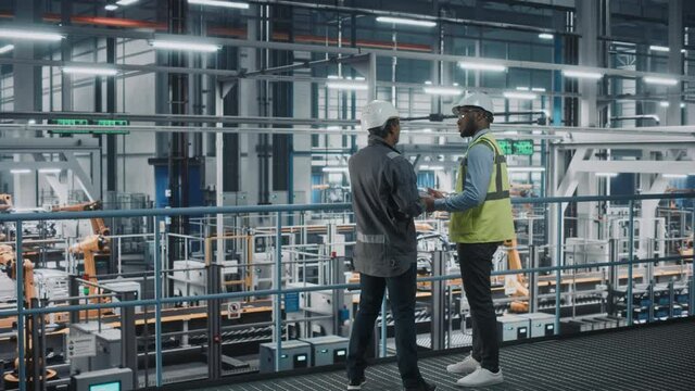 Multiethnic Manager and African American Car Factory Engineer in Uniform Using Tablet Computer. Automotive Industry 4.0 Manufacture Employees Discuss Work on Vehicle Assembly Plant.