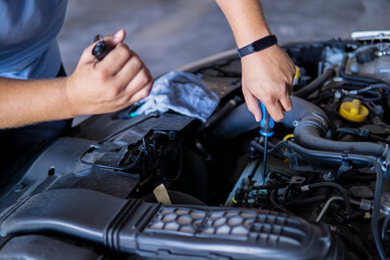 Auto mechanic working and repairing a car engine in a garage with a screwdriver and a torch.