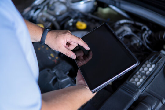 Auto mechanic with digital tablet at work making an engine repair diagnosis of a car in a mechanic garage