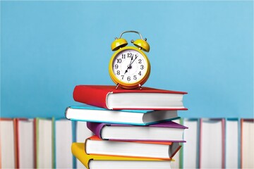 A row of colorful school books and alarm clock on background