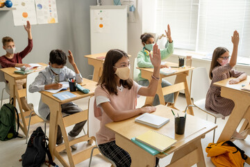 Obraz premium Clever schoolchildren of various ethnicities in protective masks raising hands