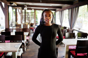 Beautiful natural young African woman with afro hair wear black dress, posed at summer terrace cafe.