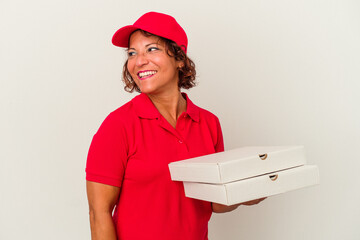 Middle age delivery woman taking pizzas isolated on white background looks aside smiling, cheerful and pleasant.