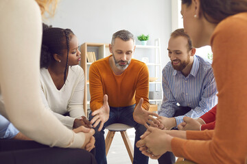Professional experienced therapist talking to diverse patients during group therapy session. Team of happy people sitting in circle and listening to psychologist or coach in informal casual meeting