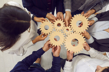 Overhead view on diverse business team people hands holding gear wheels finding working solutions. Power partnership, engineering teamwork, manage team work and company activities concept - obrazy, fototapety, plakaty