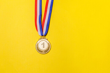 Simply flat lay design winner or champion gold trophy medal isolated on yellow colorful background. Victory first place of competition. Winning or success concept. Top view copy space.