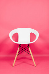 Abstract white chair with wooden legs in pink background with copy space