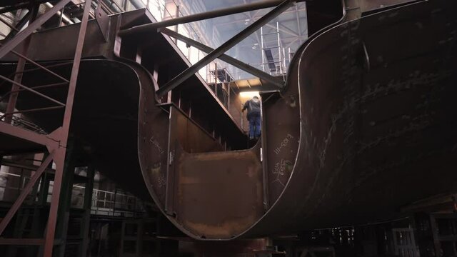 Section of old crab ship and skilled worker inside empty hold in spacious dry repairing dock at industrial complex