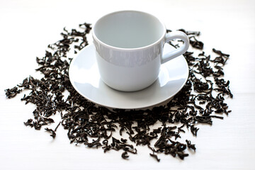 A ceramic cup and saucer with tea leaves scattered around on a white wooden table