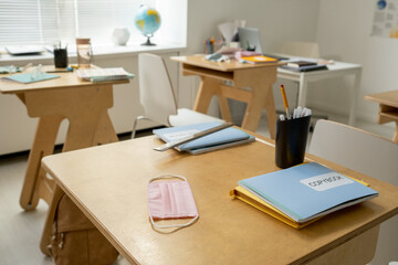 Several copybooks, protective mask and bunch of pens on wooden desk