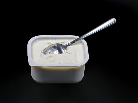 low-fat quark in plastic container with spoon isolated on black background