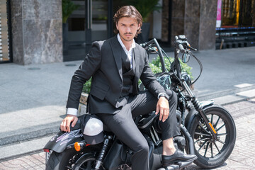 Obraz na płótnie Canvas Young brunet man in formal black suit sitting on black motorcycle.Portrait. High quality photo