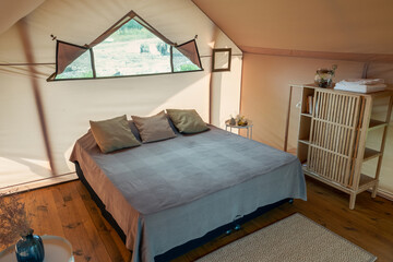 Large double bed with cushions standing on wooden floor of bedroom inside glamping house for family