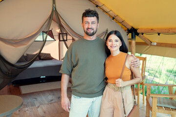 Obraz na płótnie Canvas Happy young man and woman standing against interior of their glamping house during travel