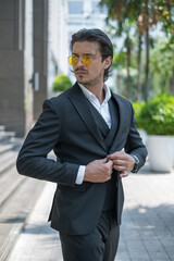 Portrait of handsome young man in black formal suit and yellow sunglasses looking aside. High quality photo