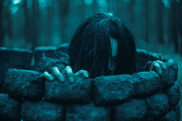 Girl in image of scary zombie crawls out of the stone well in dark forest. - obrazy, fototapety, plakaty