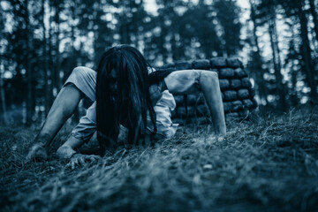 Girl in image of scary zombie crawls on ground in dark forest.