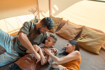 Happy parents ticking their teenage son while relaxing on bed together during travel
