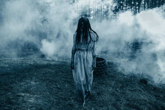 Girl in image of scary zombie walks in dark forest among smoke.
