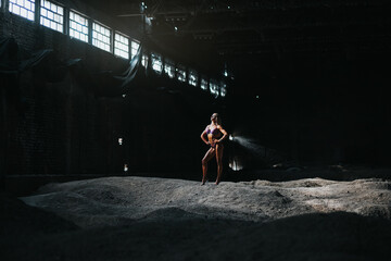 muscular female bikini fitness champion posing in abandoned hangar