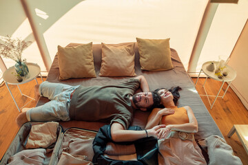 Obraz premium Happy couple daydreaming while lying on bed with unpacked baggage