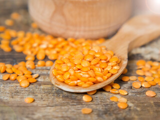 Red lentils in a wooden spoon on an old wooden table close-up. Vegetarian food.