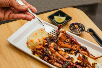 Fried squid tentacles with dried chili and garlic accompanied by white rice and rosemary, served on a white plate on a wooden background.