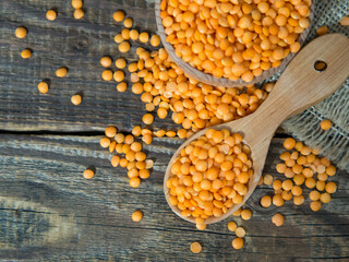 Red lentils in a wooden plate and spoon on an old rustic table. Vegetarian food.