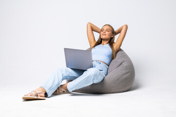 Optimistic woman sit pouf hands behind head hold laptop wear top jeans on white background